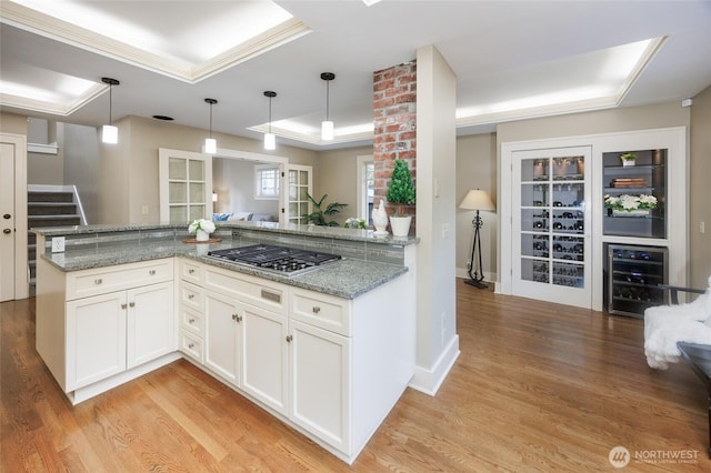 kitchen featuring stainless steel gas cooktop, wine cooler, a raised ceiling, and light wood-style flooring