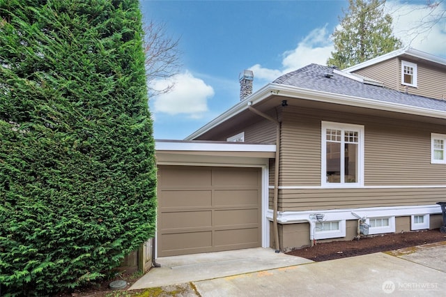 view of side of property with a garage, a chimney, concrete driveway, and roof with shingles