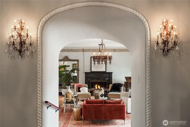 living area featuring a warm lit fireplace, a notable chandelier, and a textured wall