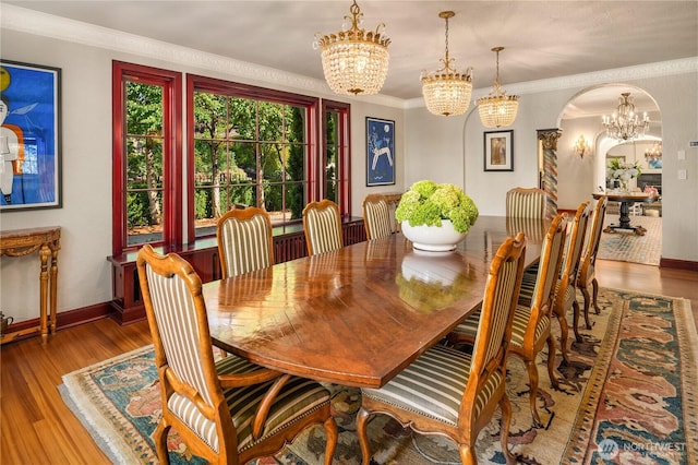 dining space with ornamental molding, arched walkways, an inviting chandelier, and wood finished floors