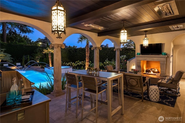 view of patio / terrace featuring a warm lit fireplace, outdoor dining area, visible vents, and an outdoor pool