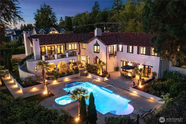 back of house featuring an outdoor living space with a fire pit, a patio, a chimney, stucco siding, and an in ground hot tub