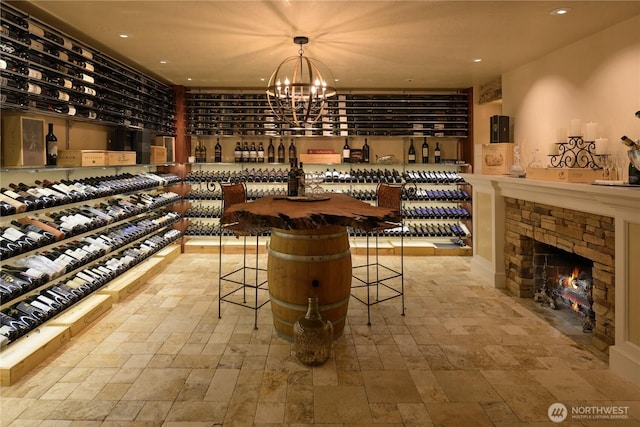 wine room with recessed lighting, stone finish floor, a stone fireplace, and an inviting chandelier