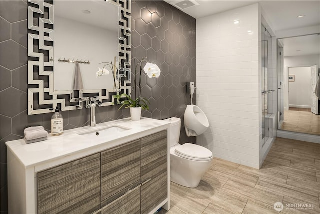 bathroom with toilet, a stall shower, vanity, and tile walls