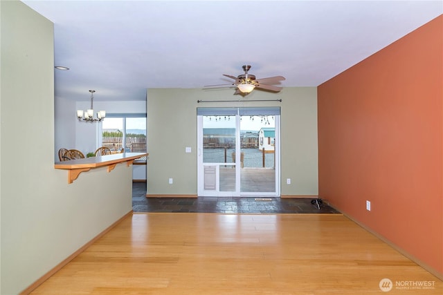 empty room featuring ceiling fan with notable chandelier, wood finished floors, and baseboards