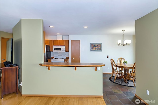 kitchen with white appliances, a breakfast bar, a peninsula, an inviting chandelier, and brown cabinets