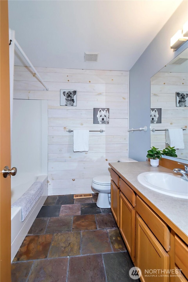 bathroom featuring visible vents, wood walls, toilet, stone tile floors, and vanity