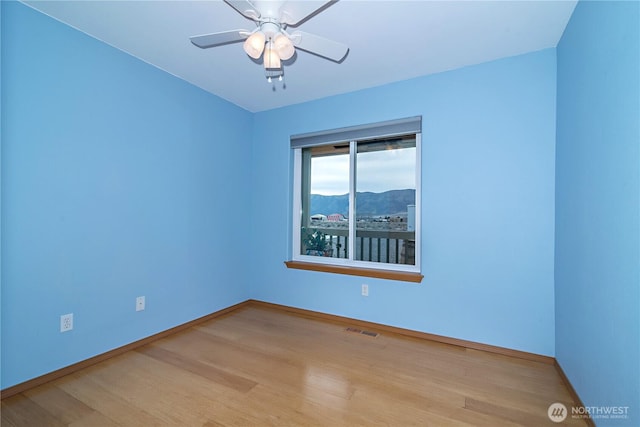 empty room featuring ceiling fan, visible vents, baseboards, and wood finished floors