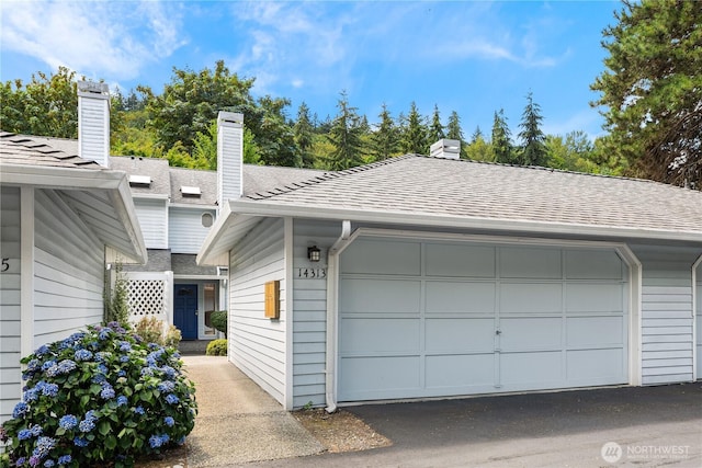 exterior space featuring a shingled roof, a chimney, and a detached garage