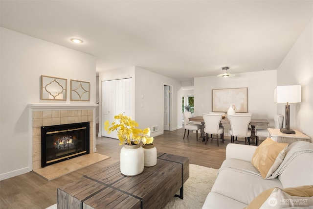 living area featuring visible vents, a tiled fireplace, baseboards, and wood finished floors