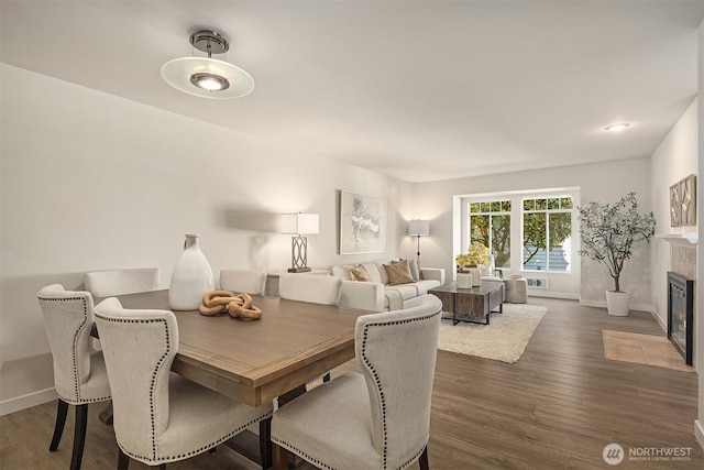 dining room featuring dark wood-style flooring, a tiled fireplace, and baseboards