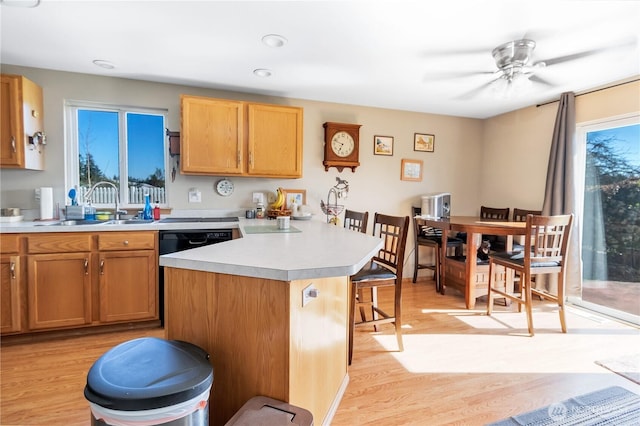 kitchen with a ceiling fan, a breakfast bar, light countertops, light wood-type flooring, and a sink