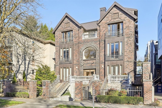 view of front of home featuring a standing seam roof, a chimney, a fenced front yard, brick siding, and metal roof