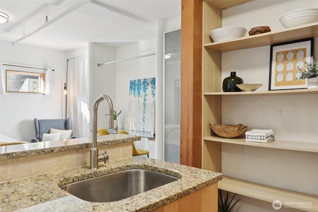 kitchen featuring open shelves, light stone countertops, and a sink