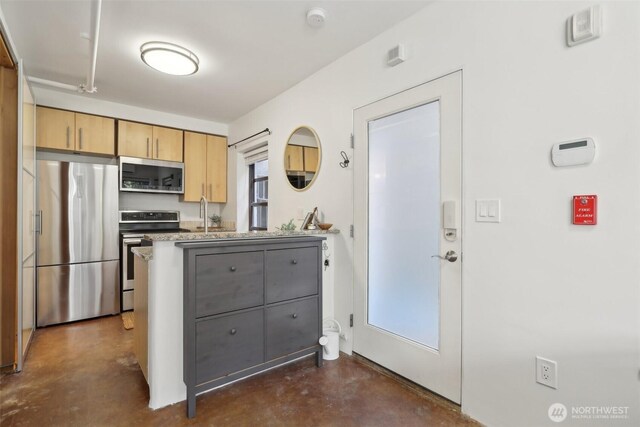 kitchen with light brown cabinets, a sink, concrete floors, appliances with stainless steel finishes, and a peninsula