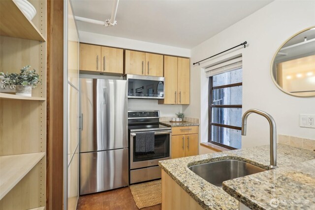 kitchen featuring a sink, light stone counters, appliances with stainless steel finishes, and light brown cabinetry