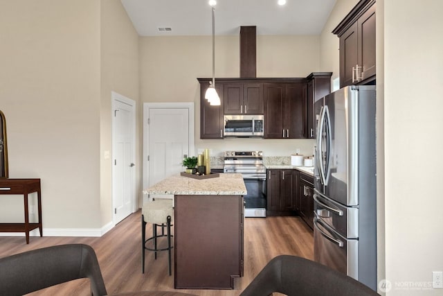 kitchen featuring light wood finished floors, a center island, dark brown cabinetry, a kitchen bar, and stainless steel appliances