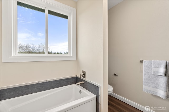 full bath featuring a garden tub, baseboards, toilet, and wood finished floors