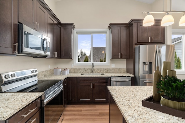 kitchen with a sink, light wood-style floors, dark brown cabinetry, appliances with stainless steel finishes, and light stone countertops