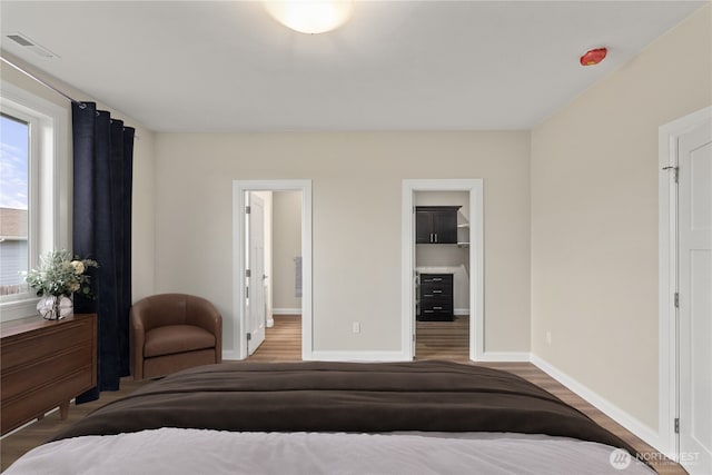 bedroom featuring visible vents, a walk in closet, baseboards, and wood finished floors