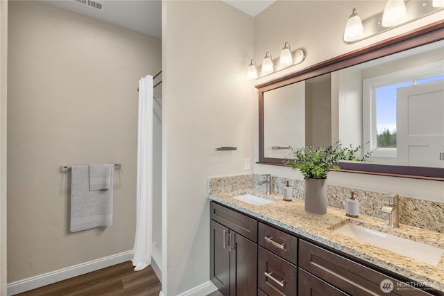 bathroom featuring double vanity, wood finished floors, baseboards, and a sink