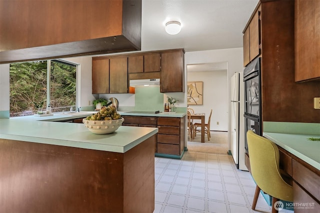 kitchen featuring light floors, a peninsula, light countertops, black appliances, and under cabinet range hood