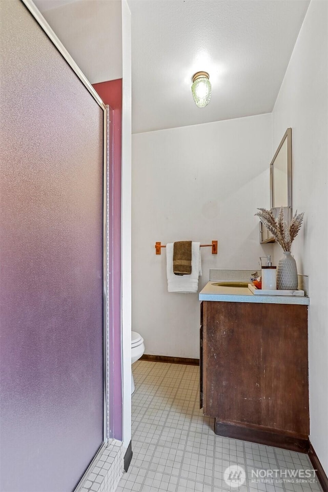 bathroom featuring baseboards, a shower stall, vanity, and toilet