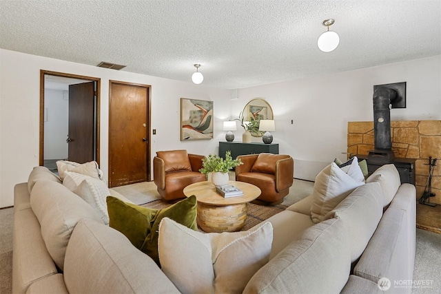 carpeted living area with a wood stove, visible vents, and a textured ceiling