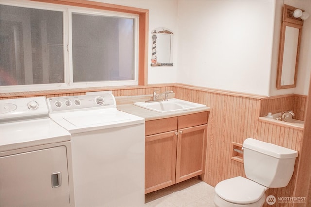 clothes washing area featuring wooden walls, a wainscoted wall, laundry area, a sink, and independent washer and dryer