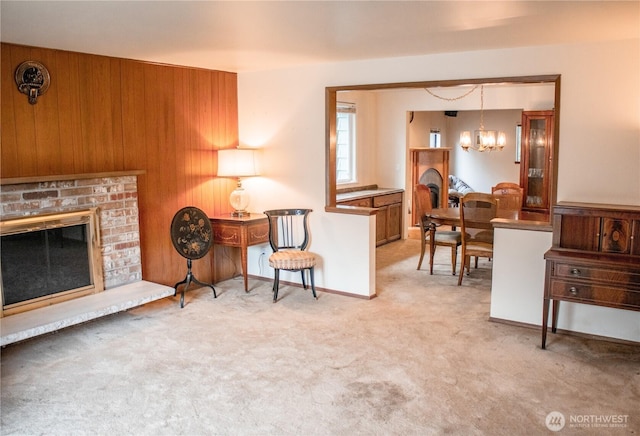 carpeted living area featuring baseboards, a brick fireplace, and a notable chandelier