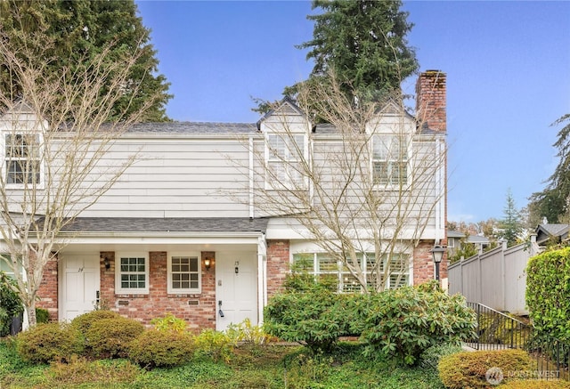 view of front of house featuring roof with shingles, brick siding, a chimney, and fence