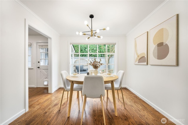 dining space with baseboards, ornamental molding, a chandelier, and wood finished floors