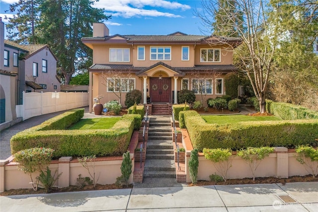 view of front of house featuring stucco siding, a tile roof, a chimney, and fence