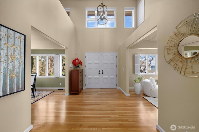 foyer entrance featuring an inviting chandelier, a high ceiling, light wood-style floors, and a wealth of natural light