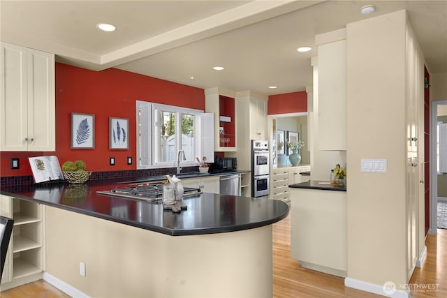 kitchen with dark countertops, a peninsula, stainless steel appliances, and open shelves