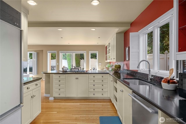 kitchen featuring dark countertops, dishwasher, light wood-style floors, refrigerator, and a sink