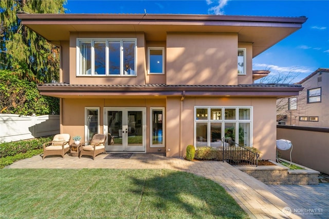 rear view of property featuring stucco siding, a lawn, fence, french doors, and a patio area