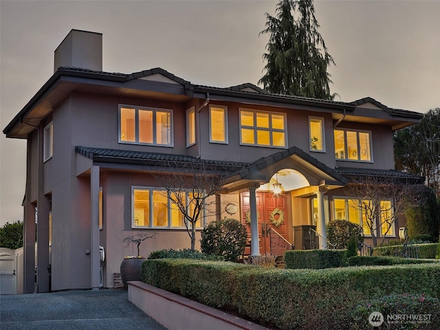 prairie-style home featuring stucco siding, a tiled roof, and a chimney