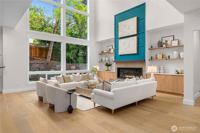 living area with a tiled fireplace, light wood finished floors, baseboards, and a towering ceiling