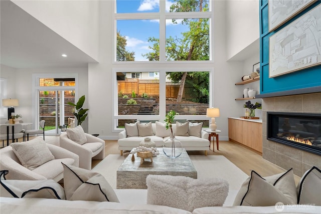 living room with a fireplace, light wood-type flooring, a towering ceiling, and baseboards