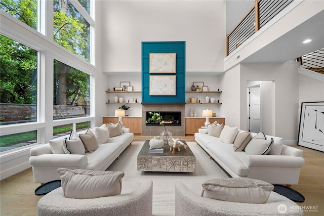 living room with a tiled fireplace, a high ceiling, wood finished floors, and baseboards