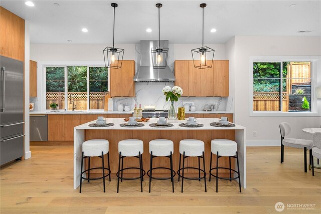 kitchen with dishwasher, a center island, wall chimney exhaust hood, and light countertops