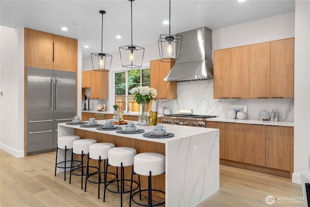 kitchen with stainless steel appliances, a kitchen island, modern cabinets, and wall chimney range hood