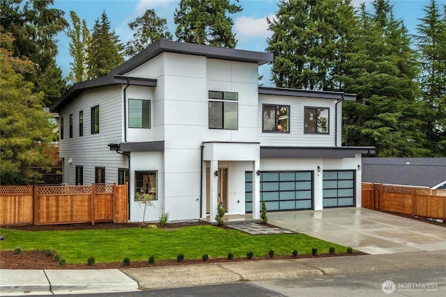 contemporary home with concrete driveway, an attached garage, fence, and a front yard