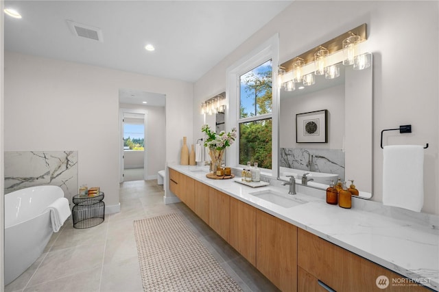 full bathroom featuring visible vents, double vanity, a freestanding tub, a sink, and tile patterned floors