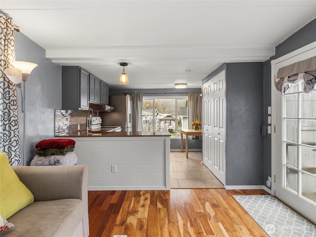 kitchen with electric range, stainless steel fridge with ice dispenser, light wood-type flooring, decorative backsplash, and dark countertops