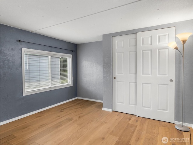 unfurnished bedroom featuring light wood finished floors, a closet, and baseboards