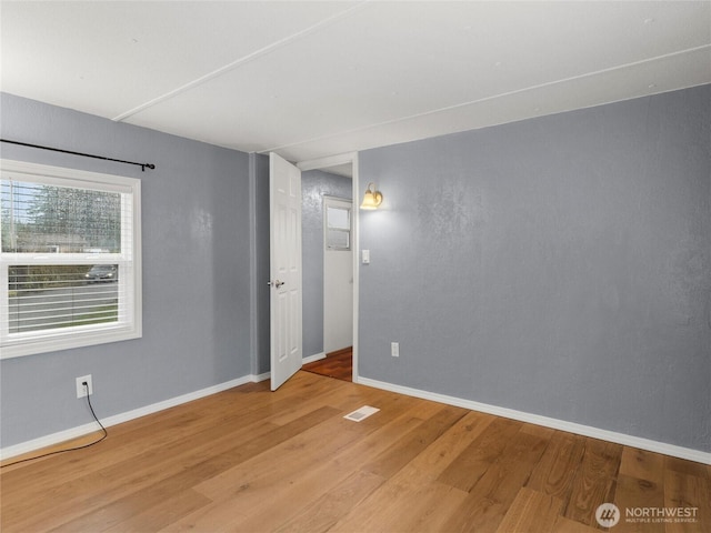 unfurnished room featuring light wood-style floors, visible vents, and baseboards