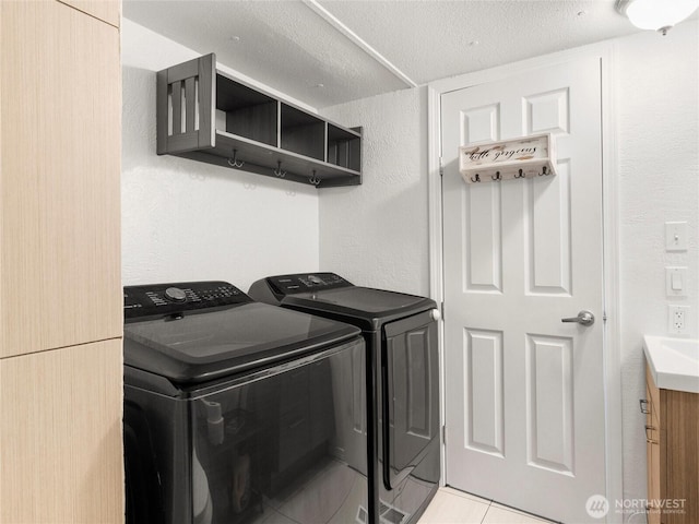 laundry area with laundry area, light tile patterned floors, washer and clothes dryer, a textured wall, and a textured ceiling