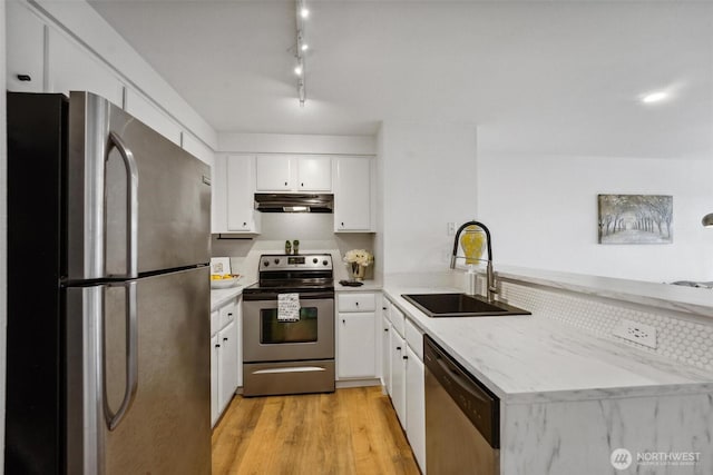 kitchen featuring light wood finished floors, appliances with stainless steel finishes, white cabinets, a sink, and under cabinet range hood